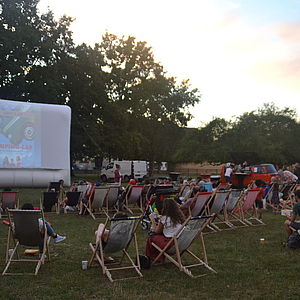 Photo du ciné plein air 2022 avec le public assis dans des transats devant un écran de cinéma dans le parc du Château Soubiran